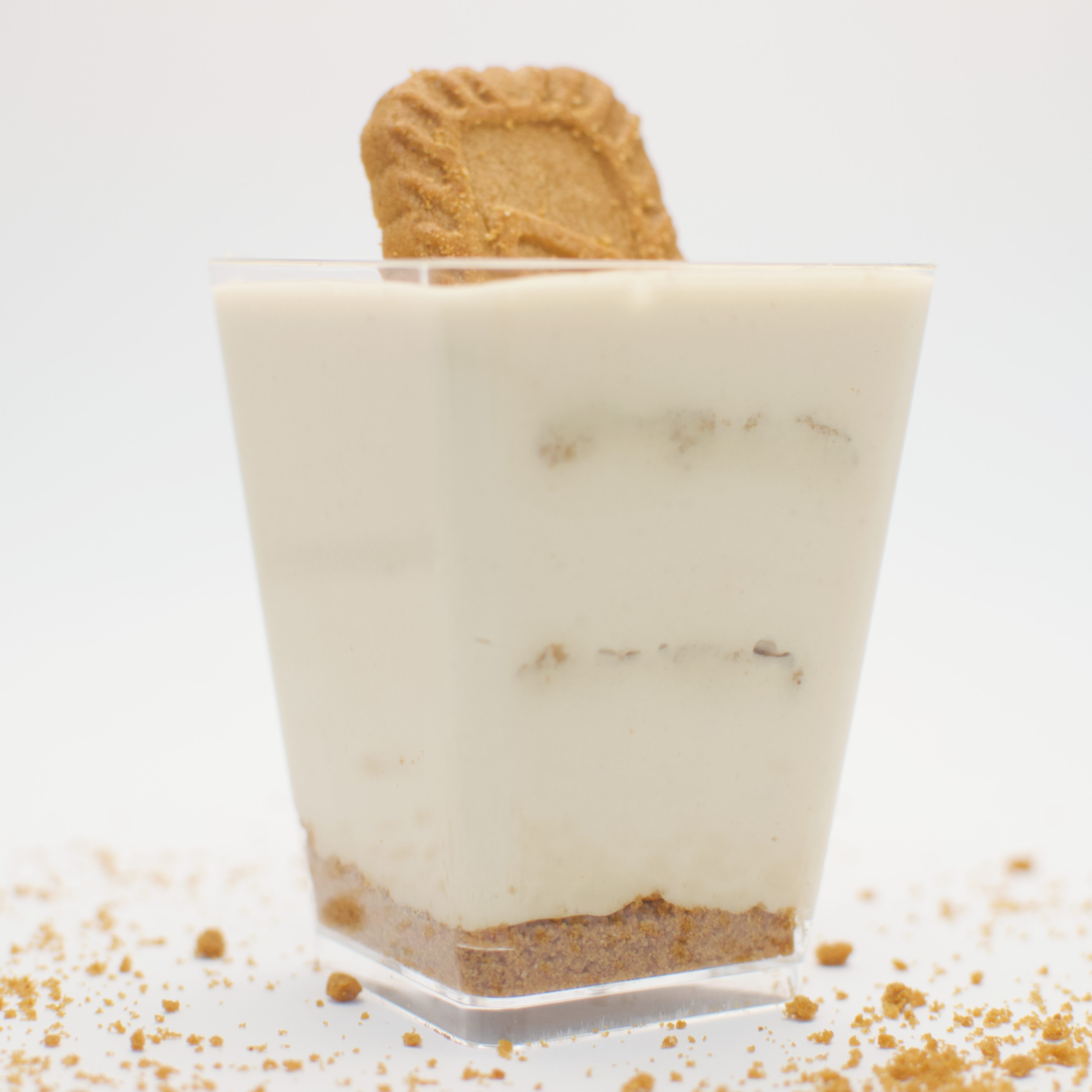 A layered dessert with golden brown crumbs and white cream on a white background, featuring a dusting of crumbs elsewhere ...